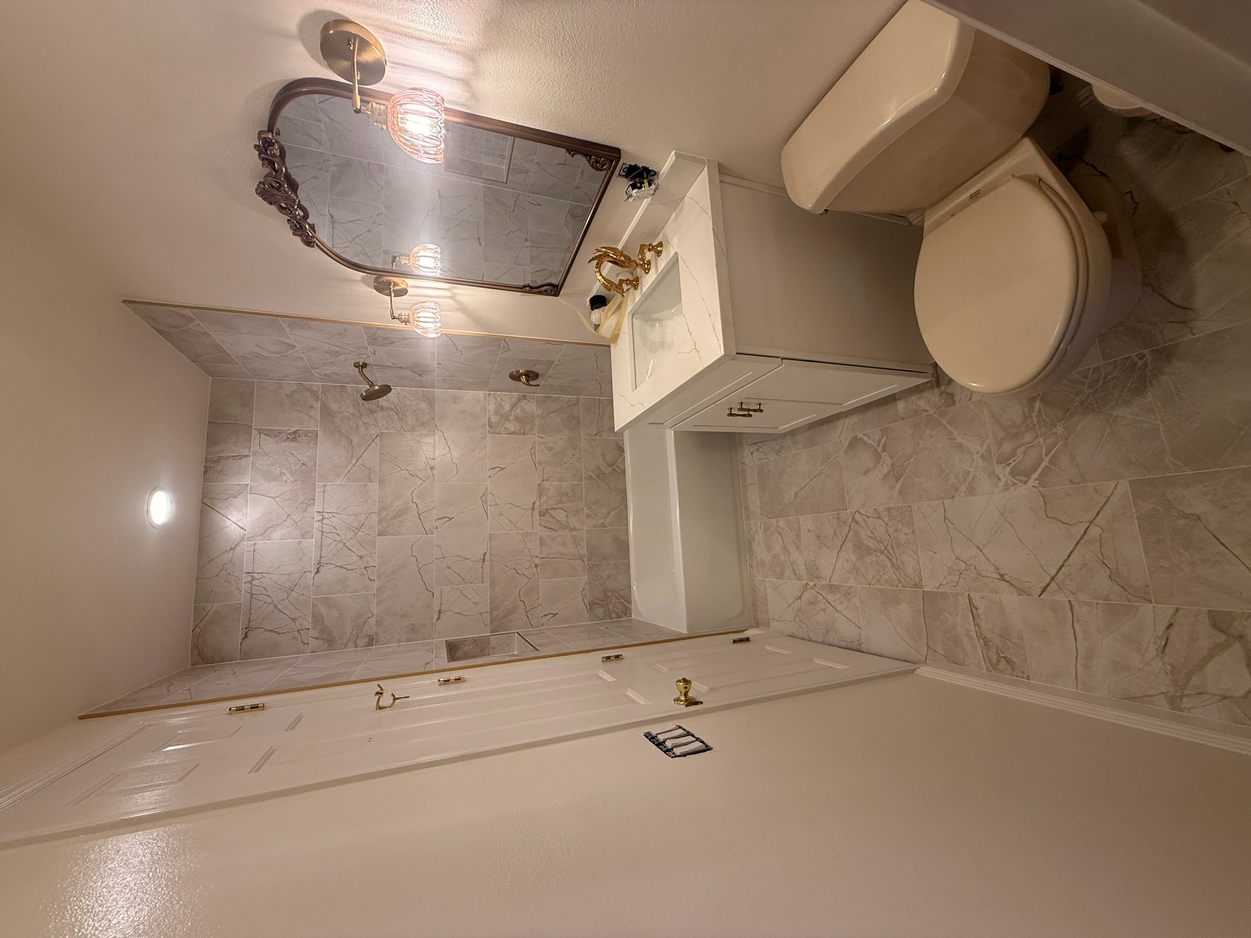 Renovated bathroom with marble tile walls, white vanity, brass fixtures, and new lighting