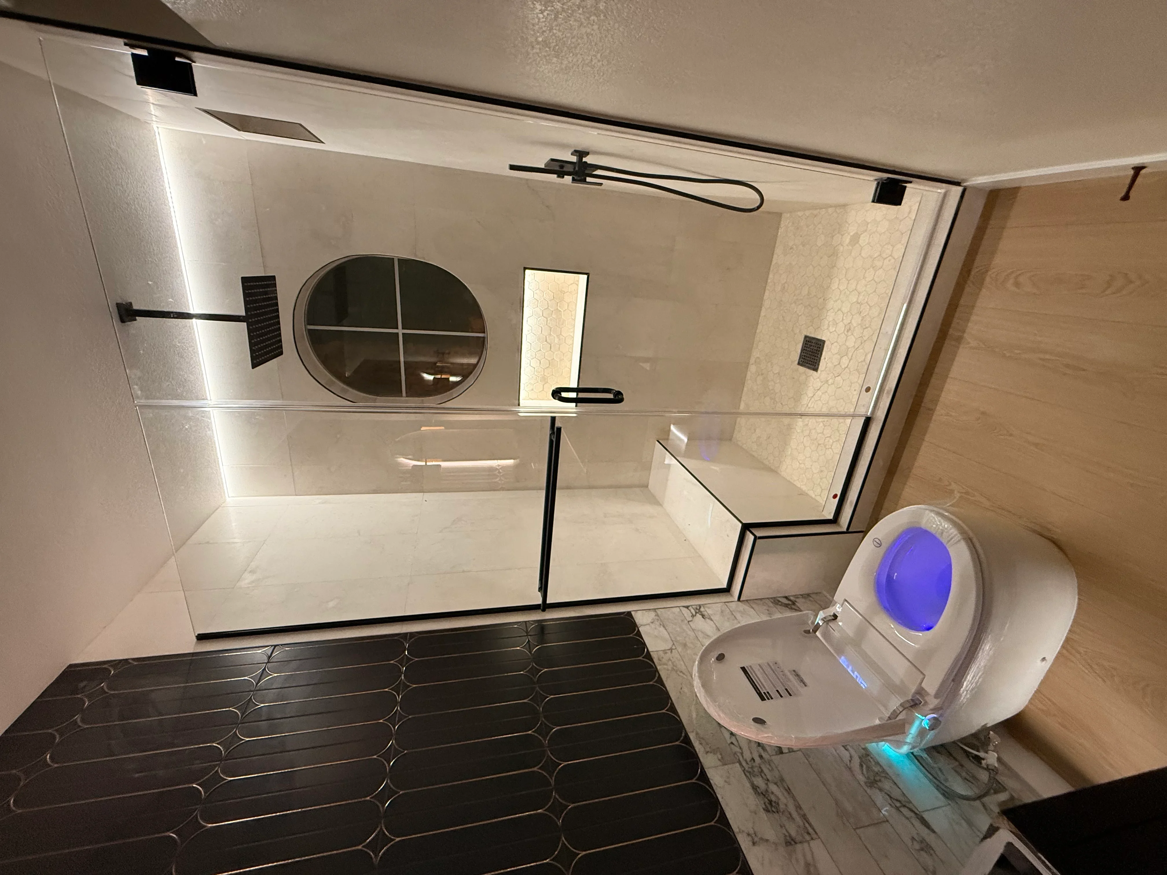 Frameless glass shower enclosure with white tile walls and geometric floor tile in modern bathroom